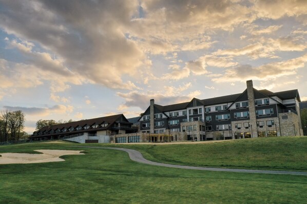 A modern hotel with multiple floors and a prominent chimney, situated on a grassy slope with a clear sky.
