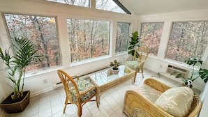 A sunlit room with large windows, wicker furniture, and potted plants. - Relaxing & Rejuvenating Retreat w/Hot tub, Pool, Sauna, & Games for family+pets (Berkeley Springs)