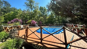 A wooden deck with a pool, surrounded by lush greenery and trees. - Relaxing & Rejuvenating Retreat w/Hot tub, Pool, Sauna, & Games for family+pets (Berkeley Springs)