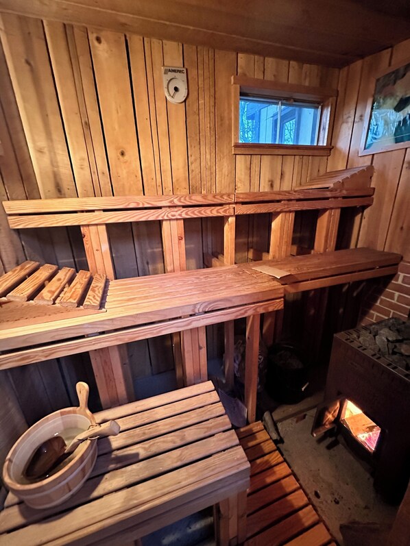 A wooden cabin interior with built-in benches, a small window, and a fireplace.