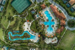 Vue aérienne d’un complexe hôtelier doté d’une grande piscine centrale, d’un court de tennis et d’une piscine sinueuse.