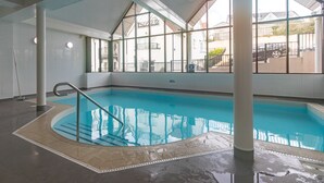 An indoor swimming pool with clear glass walls, a tiled floor, and a metal ladder. - Bryn Y Mor - Swimming Pool and  Sea Views (Tenby)