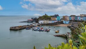 A coastal town with colorful buildings, a harbor with boats, and a prominent hill with a structure on top. - Bryn Y Mor - Swimming Pool and  Sea Views (Tenby)