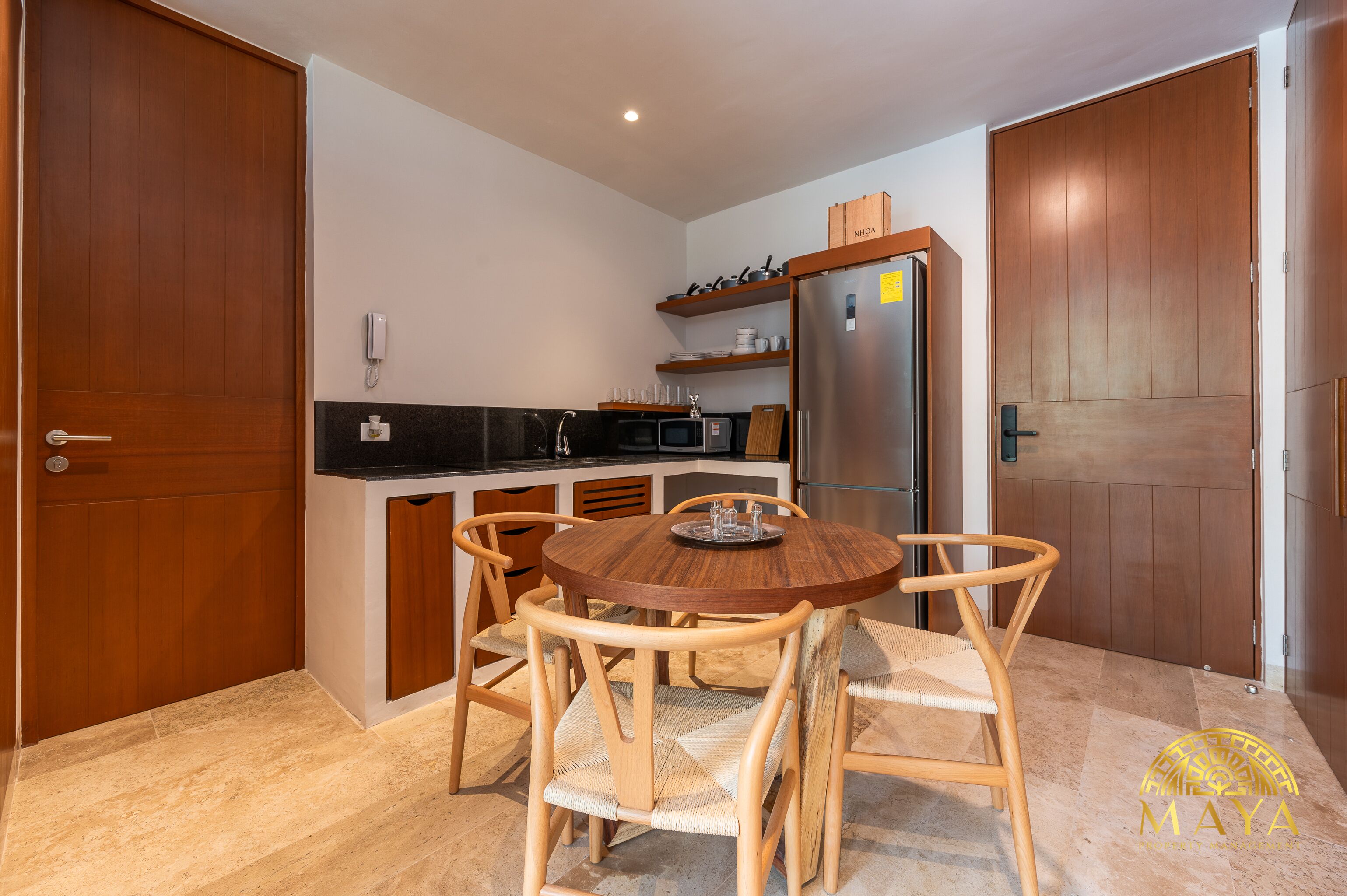 Uma cozinha compacta com uma mesa redonda de madeira e cadeiras, forno embutido, micro-ondas e frigorífico.