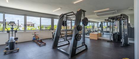 Une salle de sport équipée de divers appareils d’exercice, dotée de grandes fenêtres et offrant une vue sur la verdure.