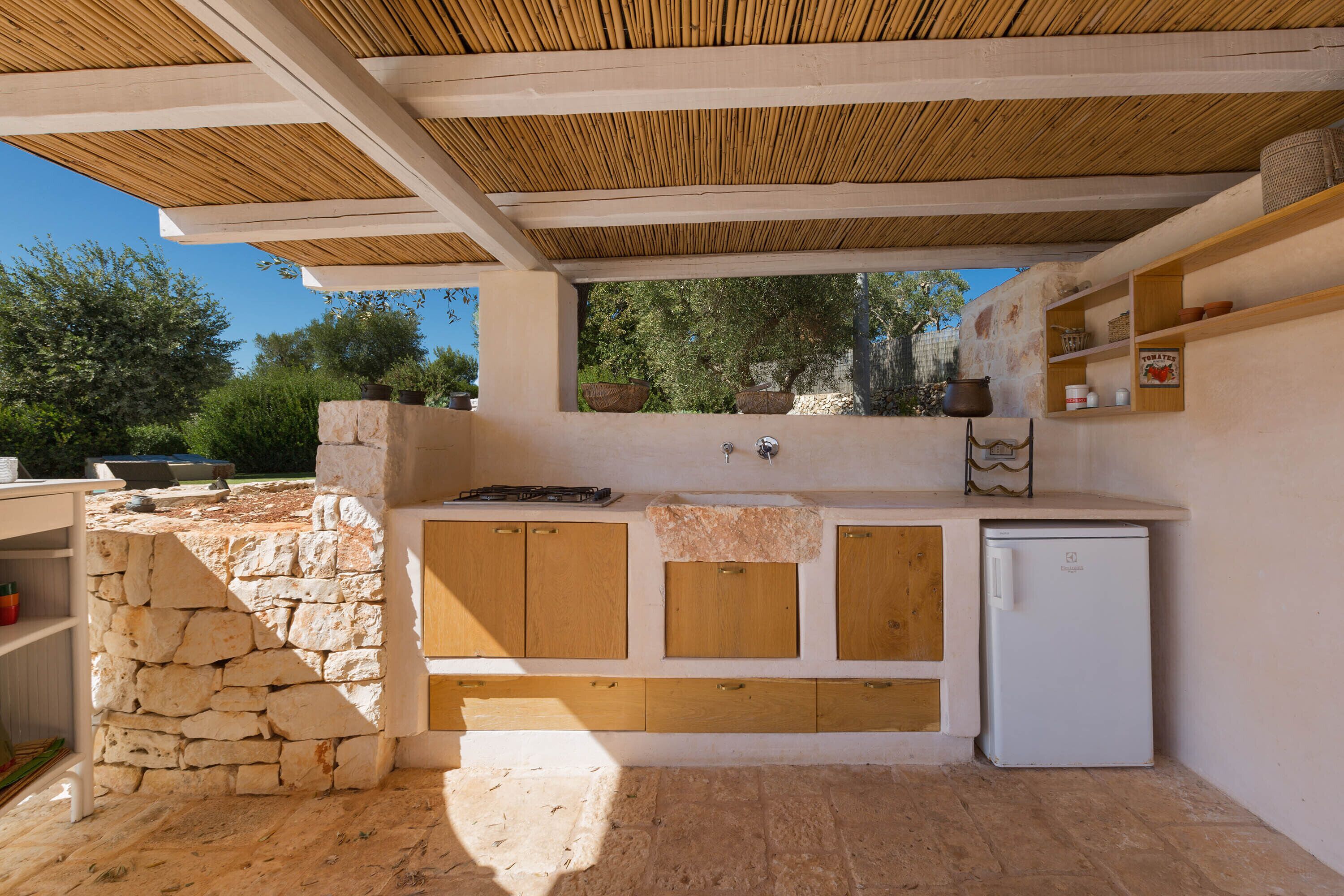 An outdoor kitchen with stone walls, wooden cabinets, and a built-in refrigerator.