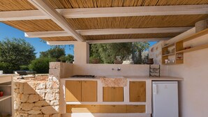 Eine Außenküche mit Steinwänden, Holzschränken und einem eingebauten Kühlschrank.