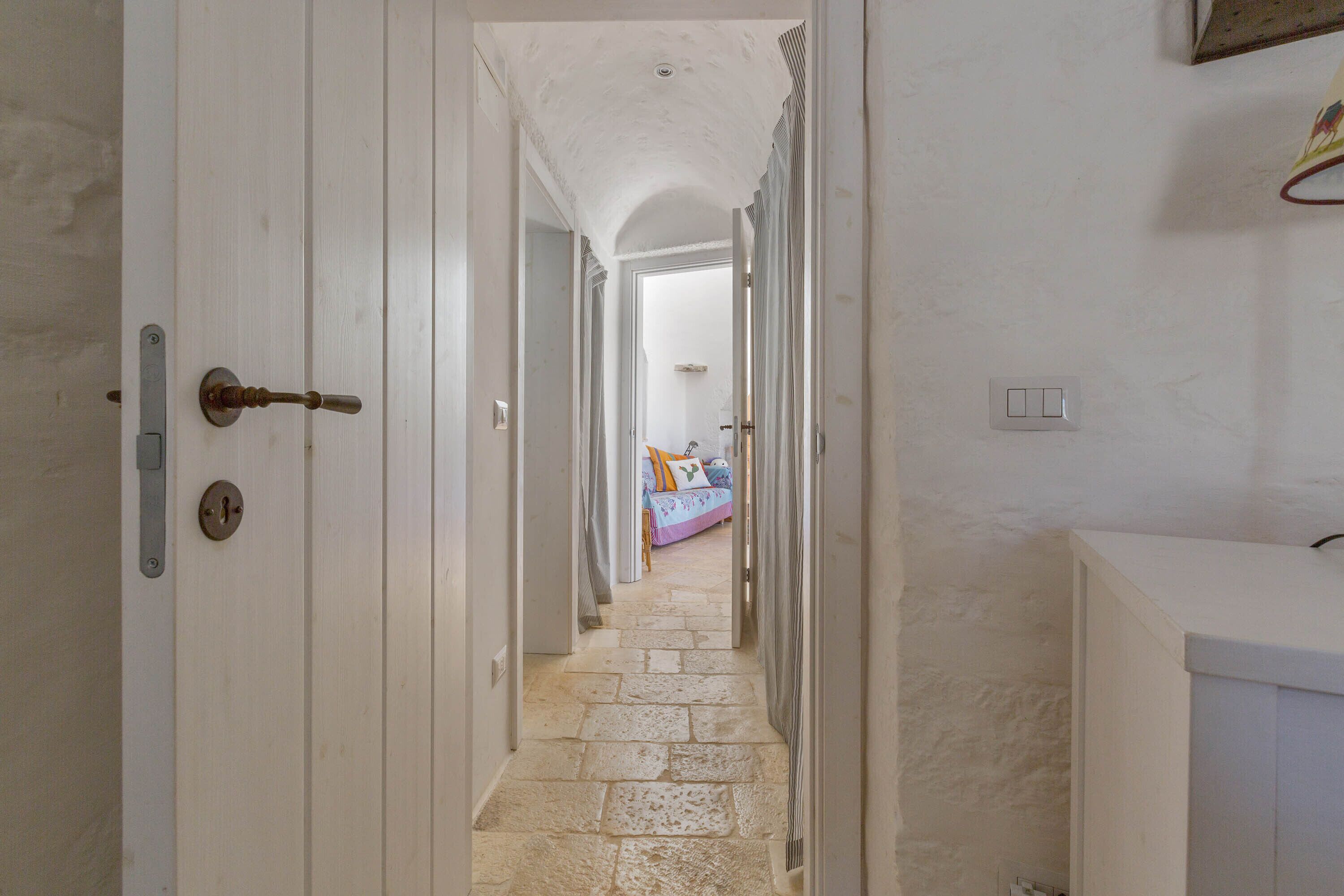 A hallway with a stone floor leading to a bedroom with a bed and curtains.