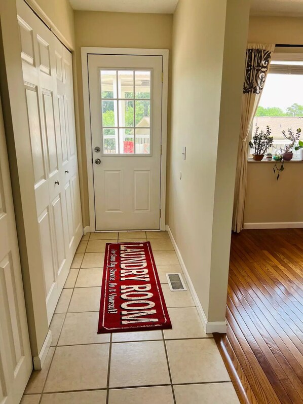 Un pasillo con un tapete rojo que dice 'Laundry Room', una puerta blanca y una ventana con cortinas.
