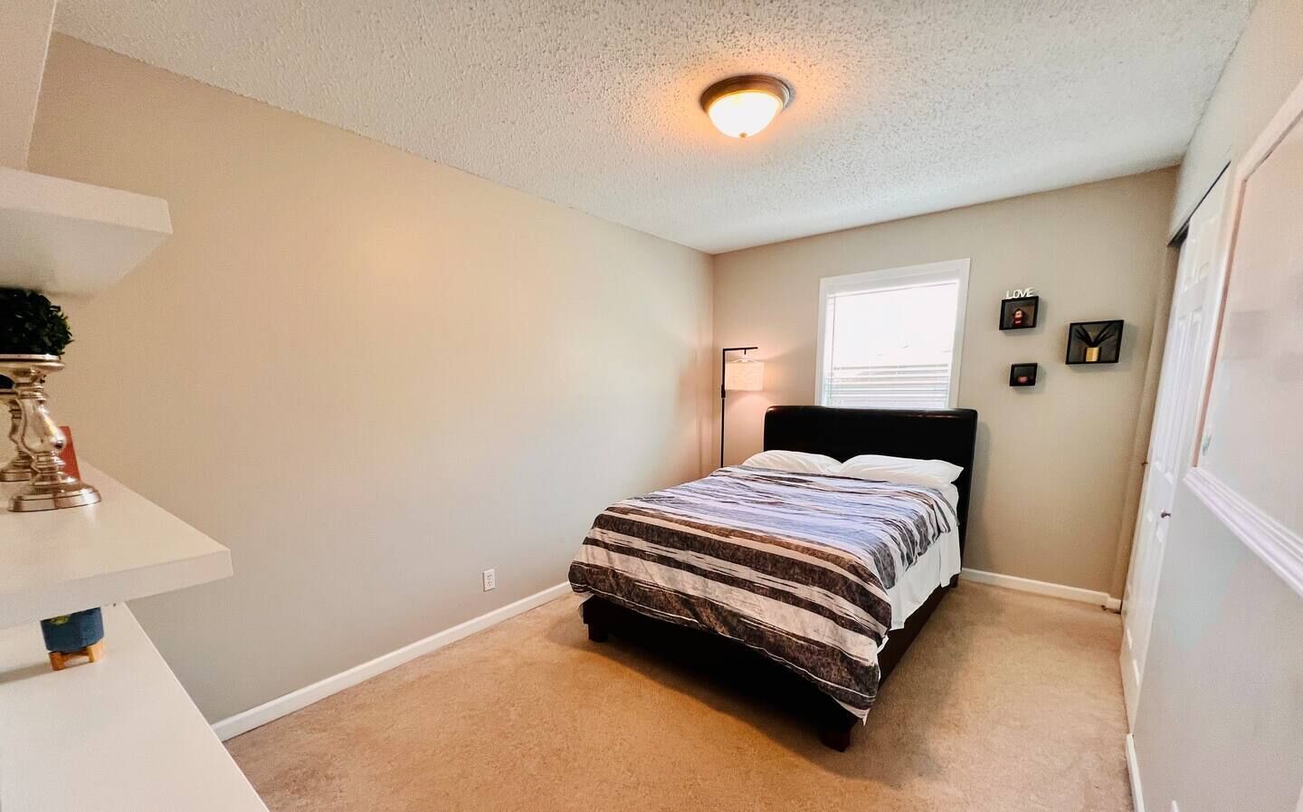 A bedroom with a bed, a nightstand, a lamp, and a window.