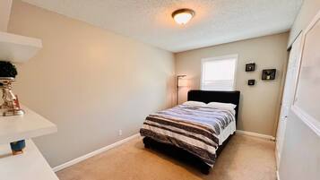 A bedroom with a bed, a nightstand, a lamp, and a window.