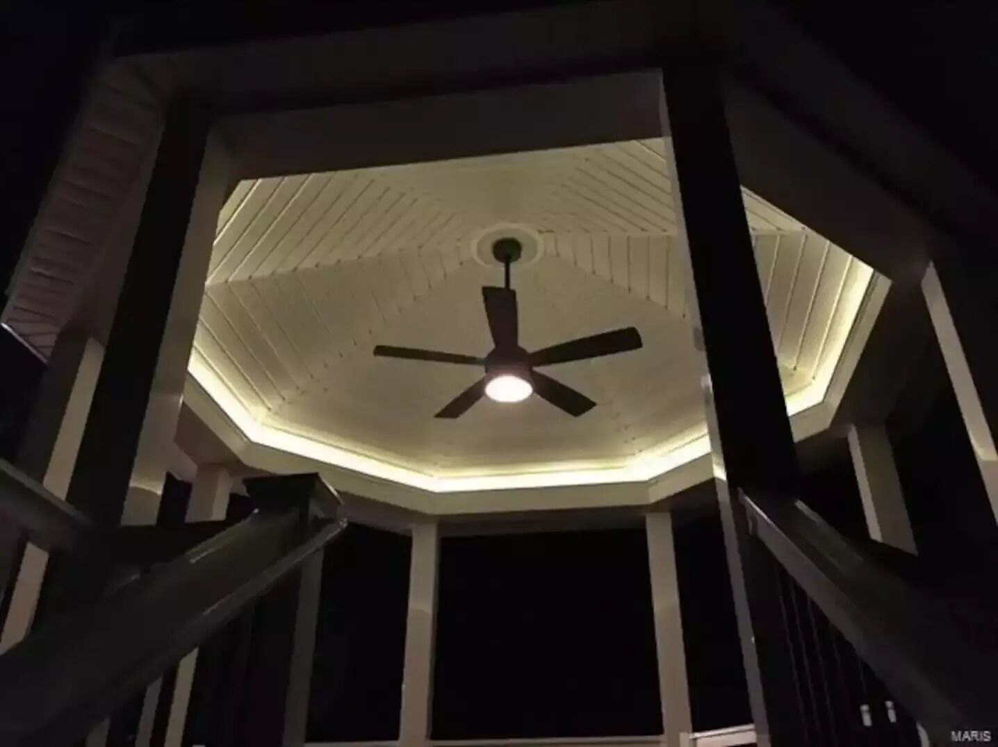 Ventilador de teto em um quarto com teto branco e vigas estruturais aparentes.