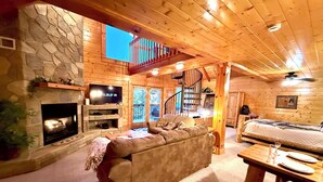 A cozy log cabin interior with a stone fireplace, a sofa, a bed, and a dining table. -  Mountain View, hot tub, pool table within 30  of downtown and national parks (Gatlinburg)