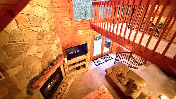 A cozy cabin interior with a stone fireplace, a television, a wooden staircase, and a couch. -  Mountain View, hot tub, pool table within 30  of downtown and national parks (Gatlinburg)