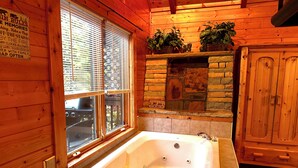 A wooden cabin interior with a large bathtub, a stone fireplace, and a window with blinds. -  Mountain View, hot tub, pool table within 30  of downtown and national parks (Gatlinburg)