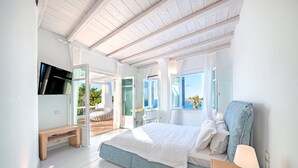 A bedroom with a bed, a bedside table, a TV mounted on the wall, and a window with a view of the outdoors. - Sanarte  Villas Mykonos (Mykonos)