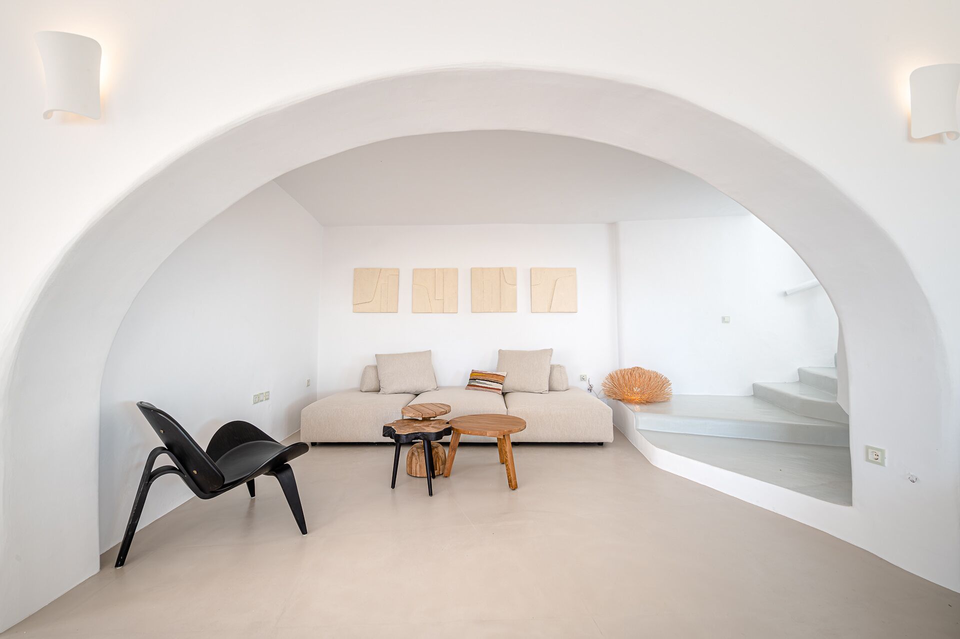 A modern interior with a curved white archway, a sofa, a black chair, and a small wooden table.