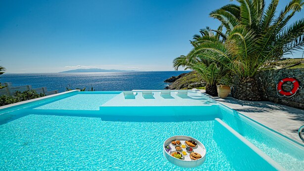A clear blue infinity pool with a view of the ocean and mountains. - Sanarte  Villas Mykonos (Mykonos)