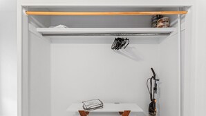 Ein weißer Kleiderschrank mit Holzregal, Kleiderstange und Staubsauger.