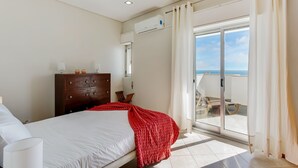 Un dormitorio con cama, cómoda y vista al mar a través de una puerta corrediza de vidrio.