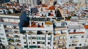 Un edificio residencial de gran altura con varios balcones, una terraza en la azotea y un entorno urbano denso.