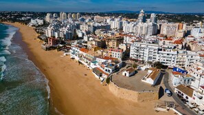 An aerial view of a coastal city with a beach, buildings, and a fortified wall. - Beach View 2BR with Balcony by LovelyStay (Armacao de Pera)