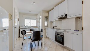 Una cocina moderna con armarios blancos, horno empotrado y microondas. Hay dos sillas y una mesa de comedor.