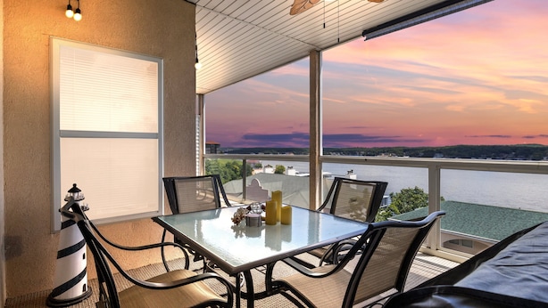 Un balcón con mesa y sillas, con vista al agua y al atardecer.