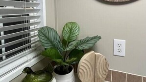 Een badkamer met een grote houten klok, een raam met zonwering, een wastafel en twee potplanten.