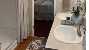 Een kleine, compacte slaapkamer met een douche, een tweepersoonsbed en een badkamer met twee wastafels.