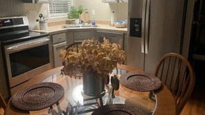 Een moderne keuken met roestvrijstalen apparatuur, een glazen eettafel en een potplante.