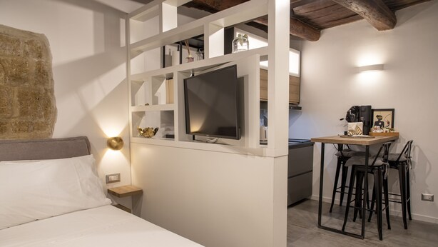 A bedroom with a bed, a bedside table, a TV, and a small kitchen area with a table and chairs. - Maritè Apartment (Naples)