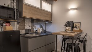 A modern kitchen with a black refrigerator, wooden cabinets, a marble backsplash, a coffee machine, and a small dining area with stools. - Maritè Apartment (Naples)