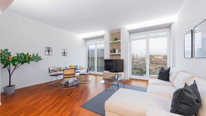 Ein modernes Wohnzimmer mit einer Couch, einem Esstisch mit Stühlen, einem Fernseher und einem Balkon mit Blick auf die Stadt.