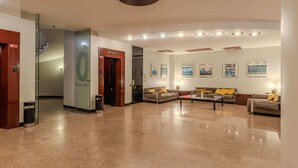 Eine geräumige Lobby mit glänzendem Boden, einer Treppe und einem Empfangsbereich mit Theke und Sitzgelegenheiten.