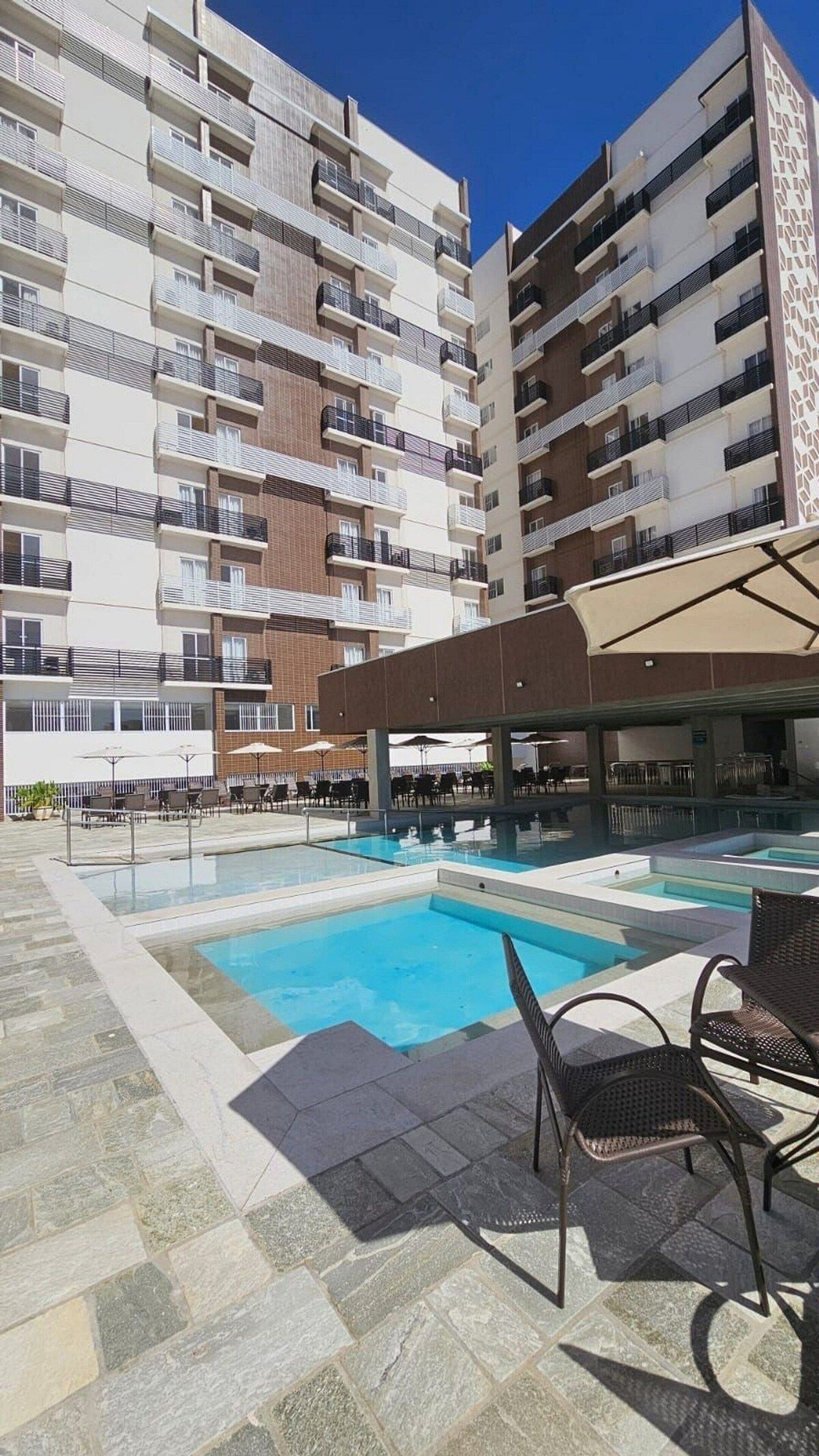 A hotel with a swimming pool, outdoor seating, and multiple balconies.
