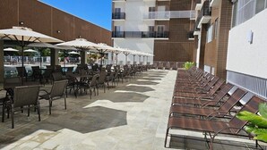 A rooftop terrace with outdoor seating and umbrellas, a swimming pool in the background, and a building with balconies. - Apartamento acesso ao diRoma Acqua Park (Caldas Novas)