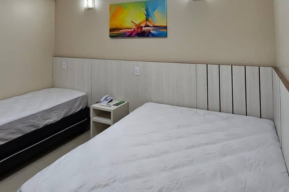 A hotel room with two beds, a skylight, a painting on the wall, and a small bedside table with a phone.