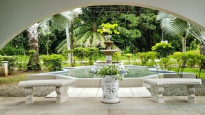 Un jardin avec une fontaine centrale, entouré de bancs et d’une végétation luxuriante.