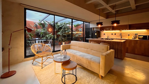 Una sala de estar moderna con un sofá, dos sillones, una mesita y un amplio ventanal corredera que da a un balcón con plantas.
