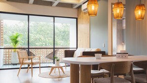 Una habitación moderna con una mesa de comedor redonda, sillas de madera, un sofá y un ventanal con vistas a zonas verdes.