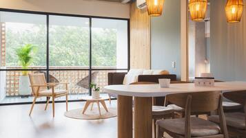 A modern room with a round dining table, wooden chairs, a sofa, and a large window with a view of greenery.