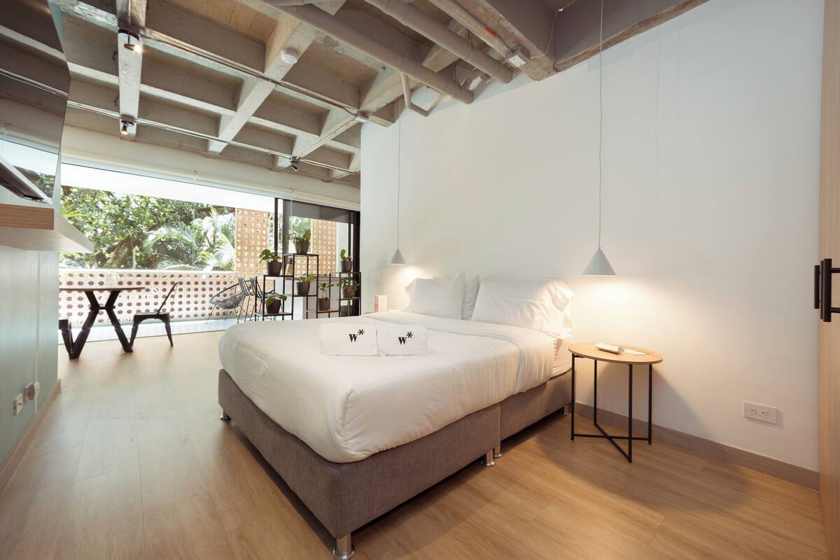 Un dormitorio moderno con una cama grande, una mesita de noche pequeña y vistas a un balcón exterior.