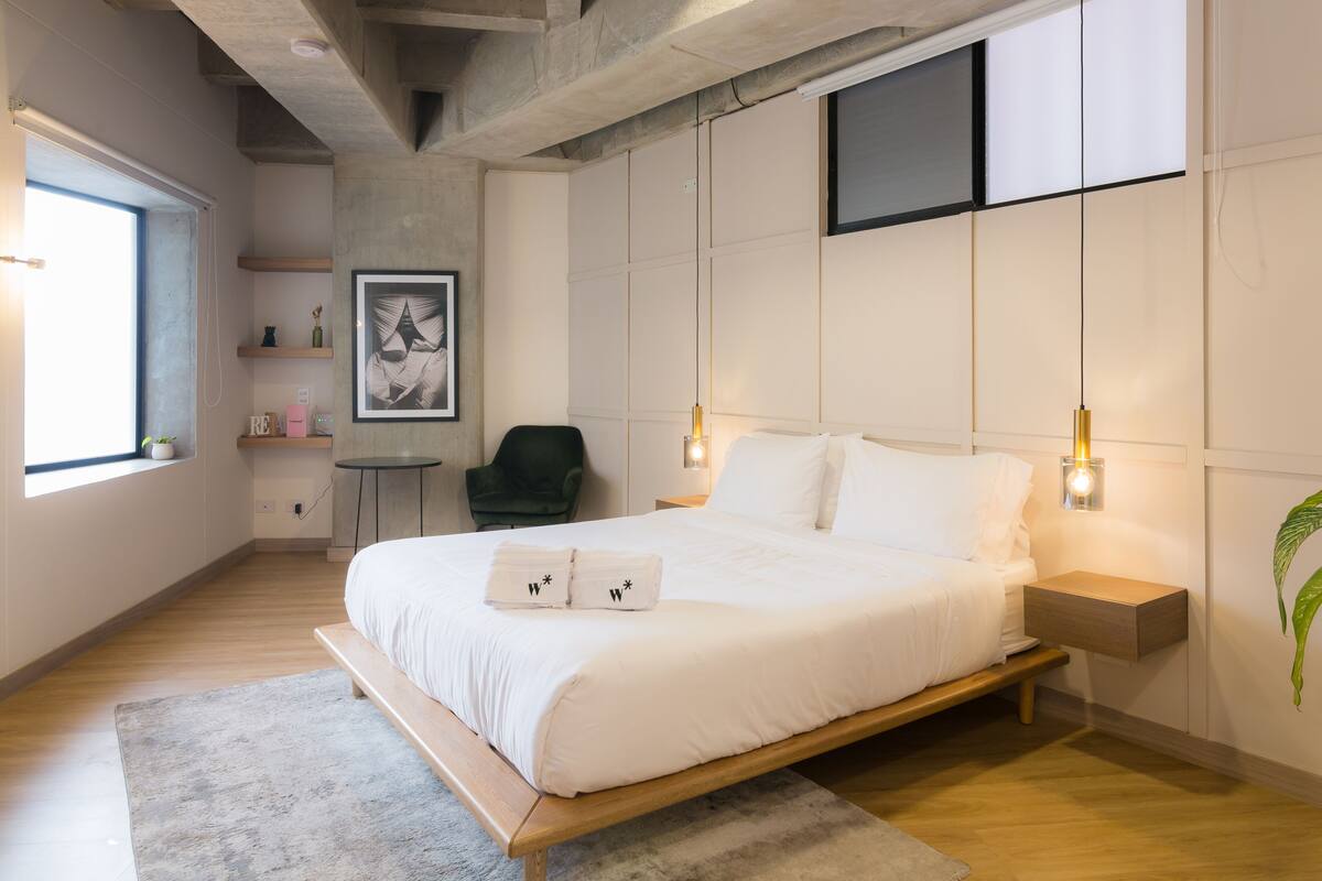 Un dormitorio moderno con una cama grande, mesitas de noche, una silla y un ventanal.