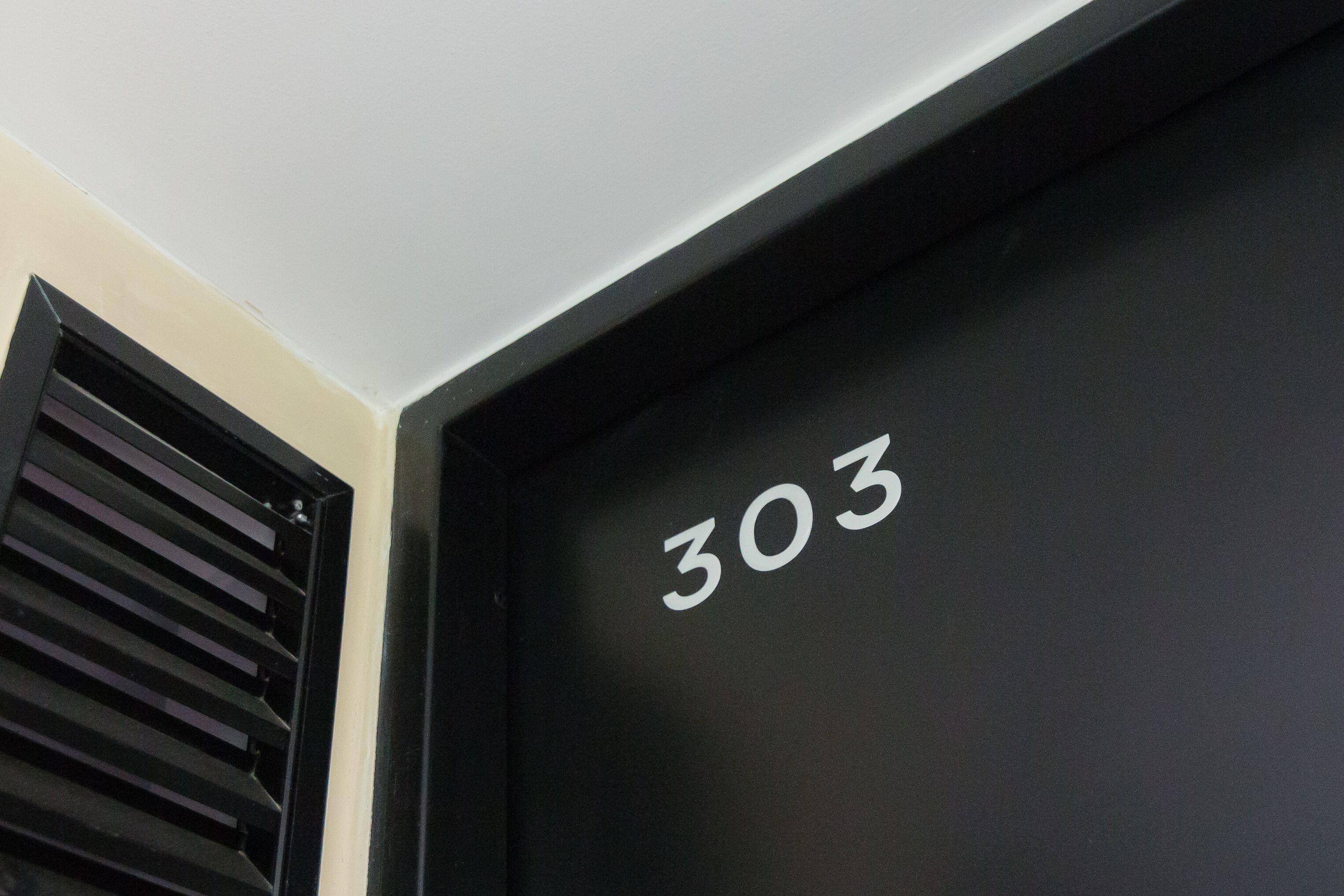Una porta negra amb el número 303 escrit en blanc.