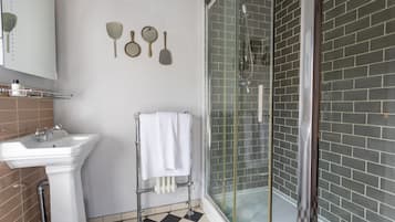 Un baño con un lavamanos blanco, una cabina de ducha con mampara de vidrio y un piso a cuadros.