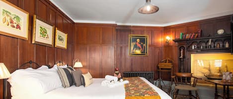 A hotel room with a large bed, wooden paneling, framed pictures on the wall, a desk with a lamp, and a ship model in a glass case.