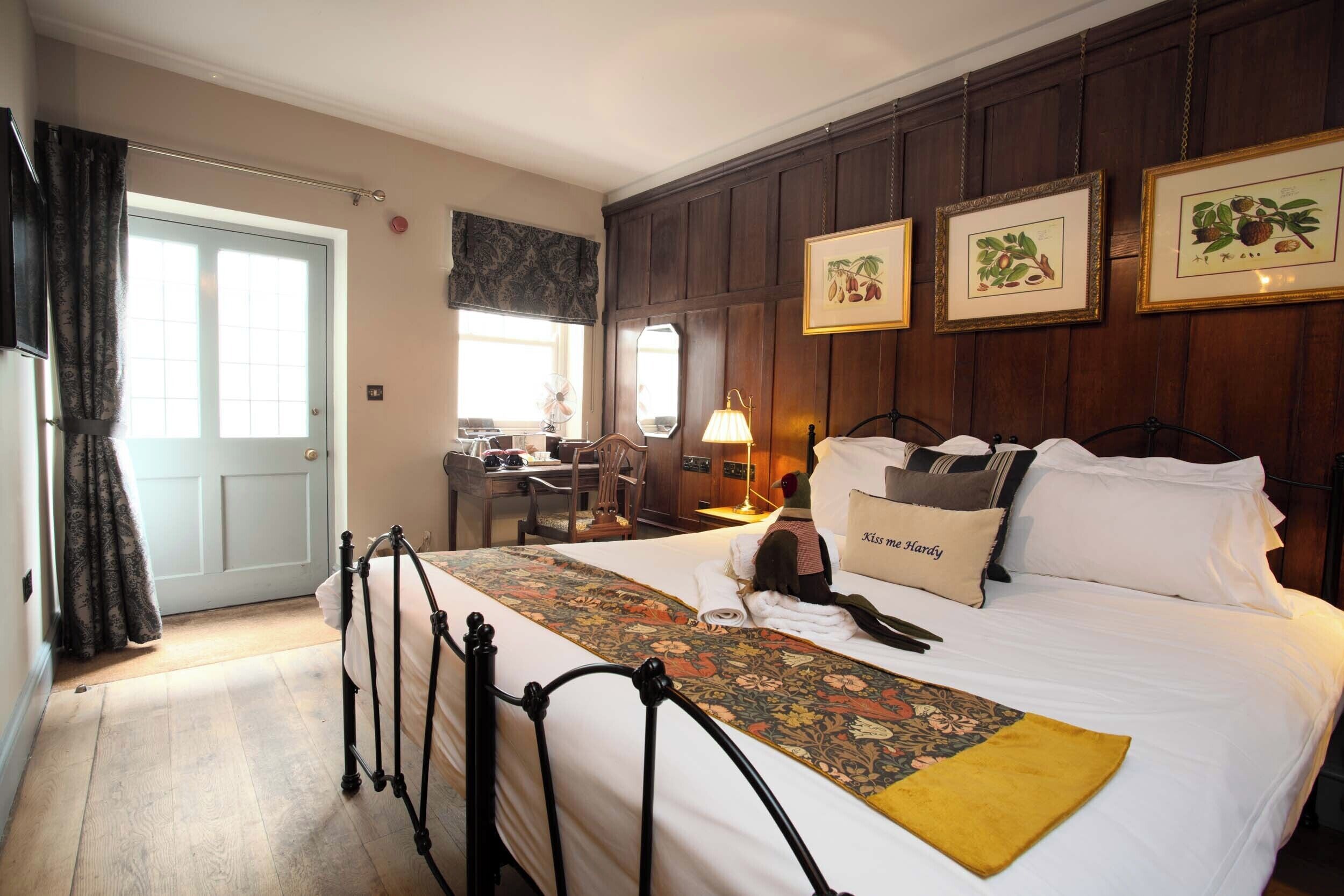 A hotel room with a bed, a desk, and a chair. There are framed pictures on the wall.