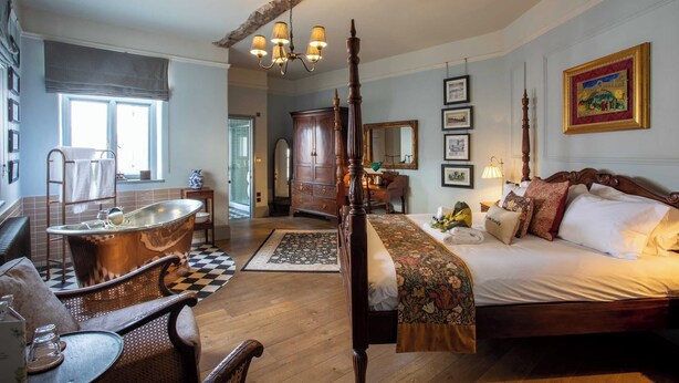 A traditional bedroom with a four-poster bed, a clawfoot bathtub, and a wooden floor. - 1777 The Albion (Wimborne)