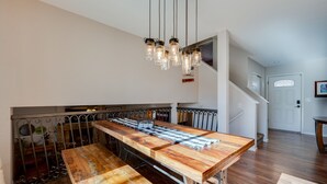 A spacious kitchen with a long wooden table, hanging pendant lights, and a staircase leading to an upper level. - Loveland Home w/ Private Hot Tub + Wood Fireplace! (Loveland)